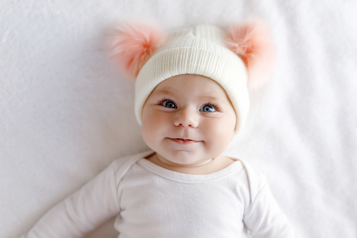 Cute adorable baby child with warm white and pink hat with cute bobbles. Happy baby girl on white background and looking at the camera. Close-up for xmas holiday and family concept.