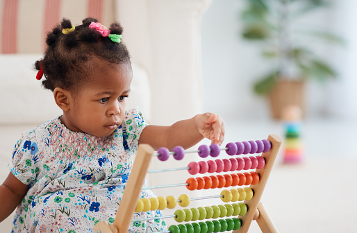 cute african american baby girl playing colorful abacus toy at home