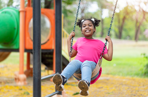 Cute African American little girl playing on swing. Smiling child playing in summer in the park. Kid in the field trips outdoor, Freedom, Happy lifestyle, Summer outdoor.
