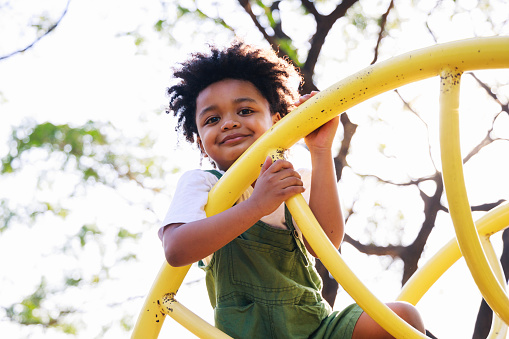 Cute African American little kid boy having fun while playing on the playground in the daytime in summer. Outdoor activity. Playing make believe concept. Outside education