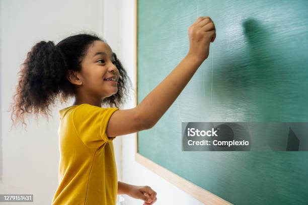 Cute African American school girl writing on blackboard and smiling