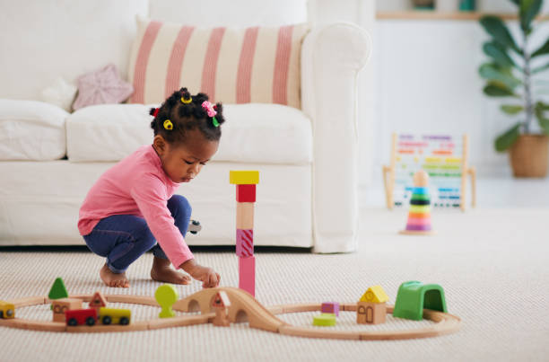 cute african american toddler baby girl playing wooden toys on the carpet at home stock photo