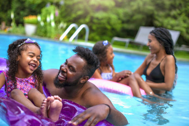 leuke afrikaans-amerikaanse familie met twee dochters die bij binnenplaatspool zwemmen - zwembad stockfoto's en -beelden