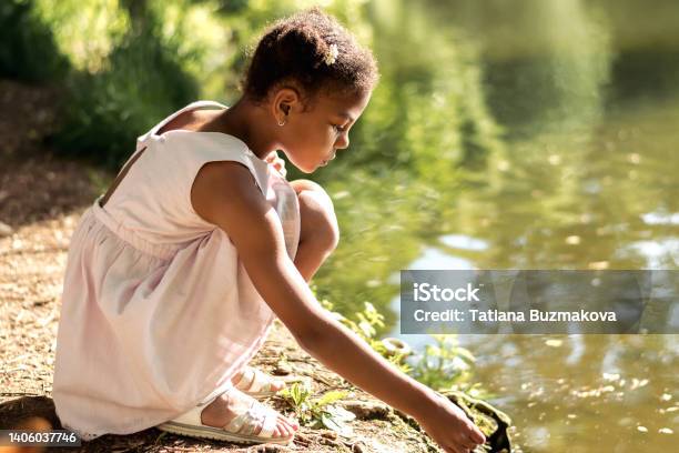 A cute African-American girl in a summer dress feeds birds on a lake on a summer day.Summer,diversity concept.