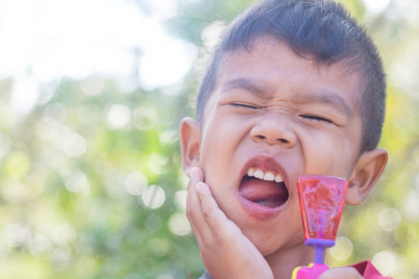 Cute Asian child eating a lollipop with sensitive teeth.  rotten teeth in children stock pictures, royalty-free photos & images