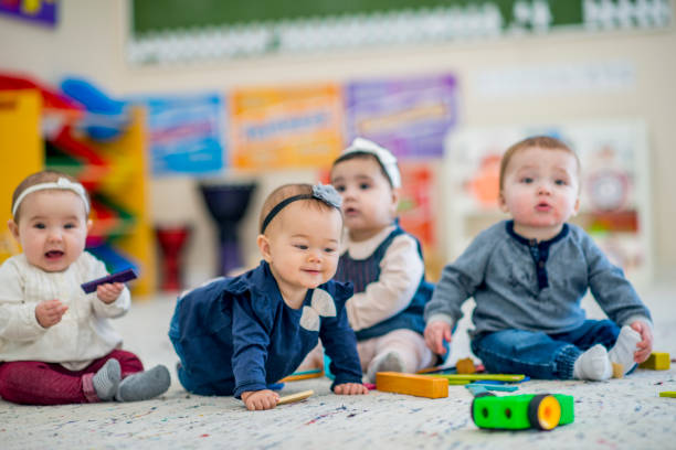 Cute babies playing with toys in daycare A 1 year old girl crawls on the carpet while smiling. A group of babies sitting next to her look around curiously. They are in a colorful daycare environment. babies only stock pictures, royalty-free photos & images