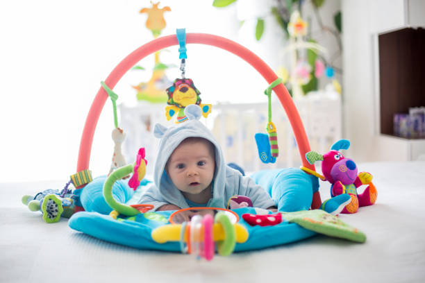 Cute baby boy on colorful gym, playing with hanging toys at home stock photo