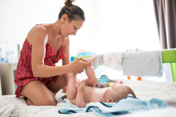 Cute baby getting his diapers changed Beautiful woman changing diaper to adorable  baby,cute boy laying on bed in the bedroom, on sunny morning tickling beautiful women pictures stock pictures, royalty-free photos & images