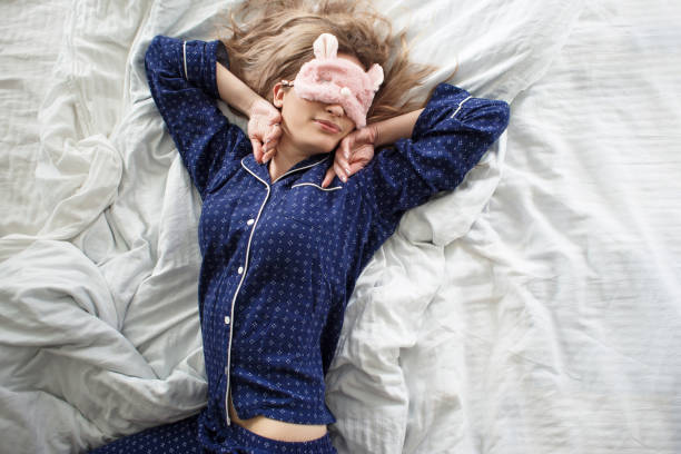 Linda rubia en su cama en pijama azul y antifaz para dormir, vista superior - foto de stock