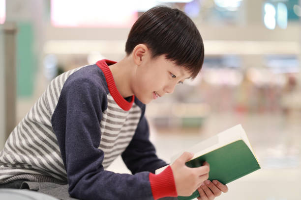 Cute boy reading book in library stock photo