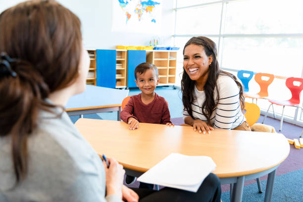 Cute boy watches mom and teacher in meeting stock photo