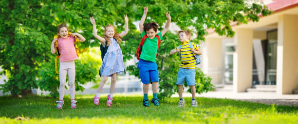Cute children with rucksacks jumping and playing in the park near the school stock photo