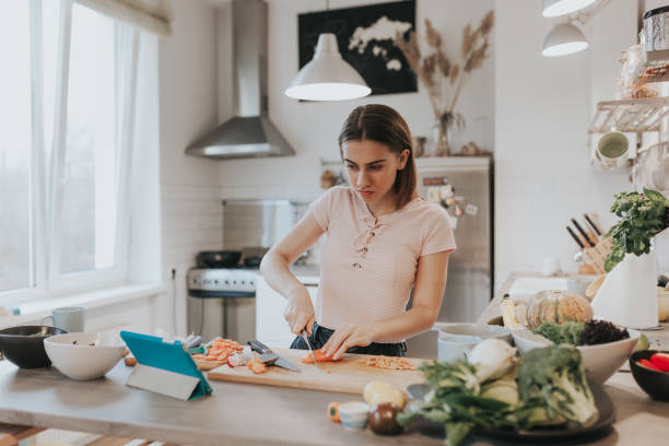 cute female teenager cooks dinner while having a video call conversation - natural food web imagens e fotografias de stock