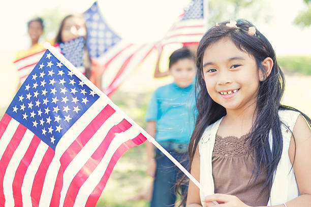 Cute Filipino girl holds American flag outdoors Beautiful Asian elementary age girl proudly holds an American flag outdoors. Her friends are holding flags in the background. philippine girl stock pictures, royalty-free photos & images