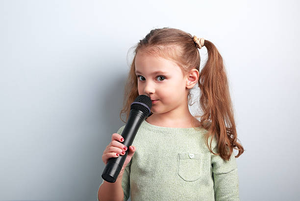 Cute fun kid girl singing in microphone on blue background stock photo