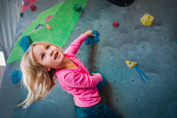 Cute girl climbing on artificial boulders wall in gym Cute small girl climbing on artificial boulders wall in gym, kids exercise bouldering stock pictures, royalty-free photos & images