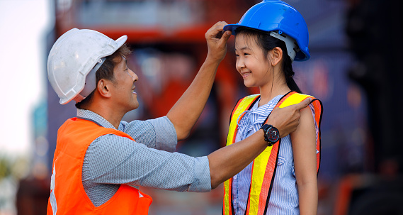 Cute girl dreams of becoming an engineer. A middle-aged male engineer wears a safety suit to his daughter with love and care. Promoting children's learning, imagination and cognitive development.