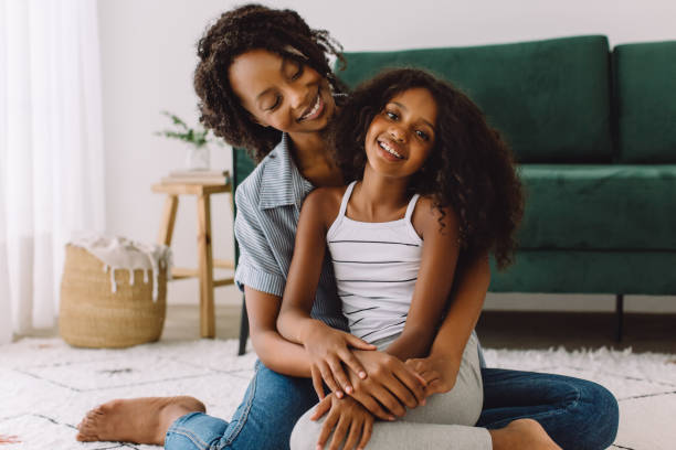 Cute girl sitting with her mother in living room stock photo