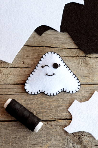Cute Halloween ghost decor, felt sheets, black thread on an old wooden table. White ghost ornament made at home. Halloween children art diy. Sewing toy. Top view stock photo