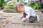 かわいらしい幸せ・好奇心が強いアジア 1 年/18 ヶ月古い幼児赤ちゃん男の子子供保持/彼の手の石と遊ぶ美しい花庭園に座って
