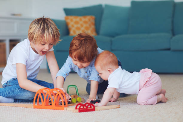 cute kids, siblings playing toys together on the carpet at home stock photo