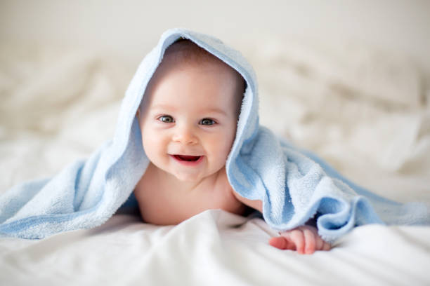 Cute little baby boy, relaxing in bed after bath, smiling happily stock photo