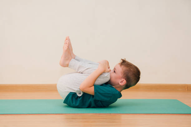 cute little boy is learning to do yoga in the gym - yoga crianças imagens e fotografias de stock