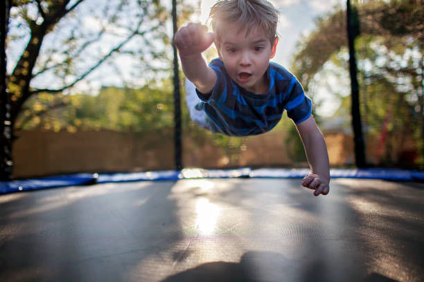 bambino carino che salta sul trampolino come un supereroe, le persone si godono la vita dopo il lockdown - tappeto elastico foto e immagini stock