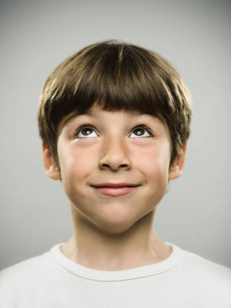 Cute little boy looking up Close up portrait of cute little boy looking up. Vertical shot of real young boy against gray background in studio. Photography from a DSLR camera. Sharp focus on eyes. looking up stock pictures, royalty-free photos & images
