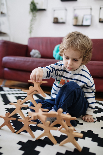 Cute little boy playing with wooden toy on the floor at home