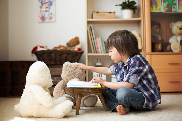 Cute little child, preschool boy, reading a book Cute little child, preschool boy, reading a book to his teddy bears at home, sun rays coming through window, dust in the air teddy ray stock pictures, royalty-free photos & images