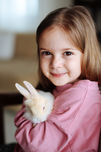 A close up portrait of a 6 year old girl hugging her pet rabbit.