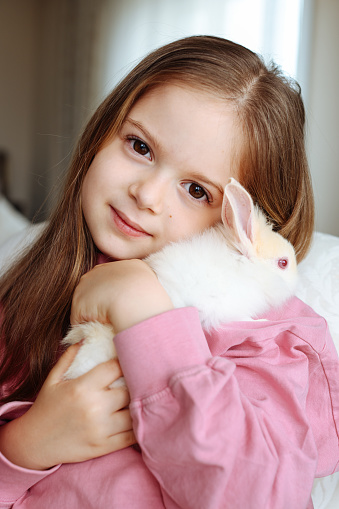 A close up portrait of a 6 year old girl hugging her pet rabbit.