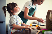 Cute little girl baking at home with mom, young mother and daughter making cookies in the kitchen.