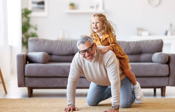 Cute little girl granddaughter playing and having fun with active positive grandfather at home stock photo