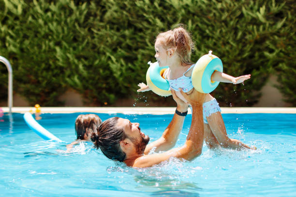 Cute little girl having fun with parents in pool stock photo
