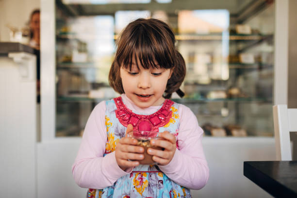 A cute little girl holding a glass of chocolate mousse while standing in a pastry shop stock photo