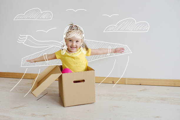schattige kleine meisje spelen met kartonnen vliegtuig in de woonkamer - fantasie stockfoto's en -beelden