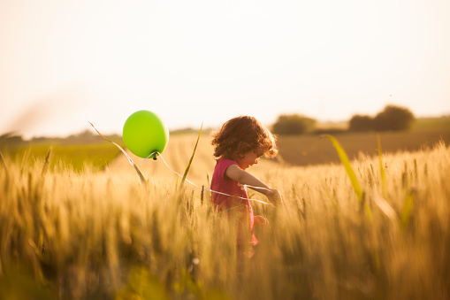 Cute little girl holding balloons and running through field