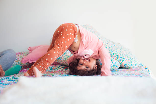 Cute portrait of happy little toddler girl playing upside down. adorable baby girl stand on head on the bed at home,smiling and having great time,happy and relaxed childhood concept 2 3 years stock pictures, royalty-free photos & images