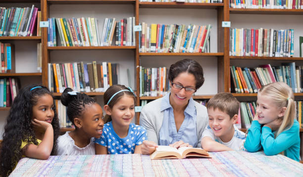 Cute pupils and teacher reading in library stock photo