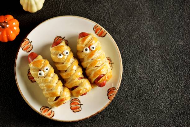 Cute sausages in puff pastry  "Mummy" with ketchup and mustard  for the Halloween party. Children's food. stock photo