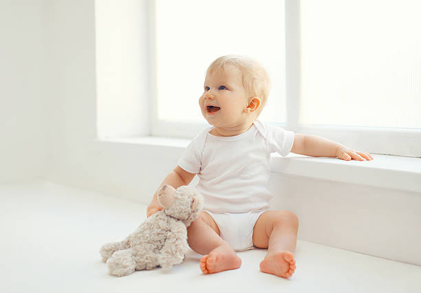 Cute smiling baby with teddy bear toy home in room stock photo
