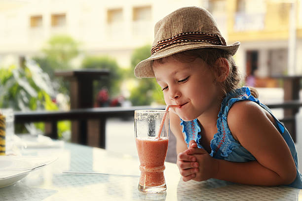 Cute thinking kid girl drinking tasty juice in street restaurant stock photo