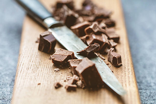 Cutting Chocolate Chunks cutting milk chocolate and dark chocolate into pieces with a knife on a wooden cutting board. dark chocolate stock pictures, royalty-free photos & images