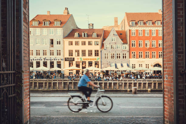 Cyclist driving past Nyhavn riverbank with historical houses and restaurants of city leisure area stock photo