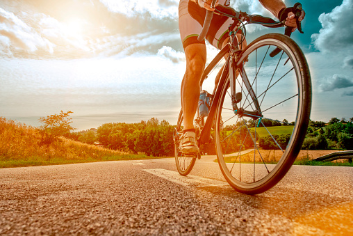 Close up of a athlete who rides his bike up a steep hill. The sun shines as his feet hits the pedals and he drives the bicycle forward.