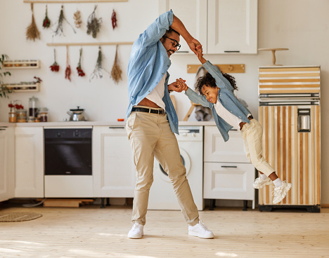 Young positive loving african american man father playing with child at home on weekend, dad spinning his son in the air while playing together and having fun, standing in modern kitchen