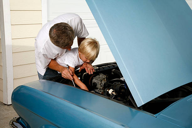 Dad Teaching Son to Fix Antique Car This is a photo of a dad teaching his son how to fix an old blue car that can relate to relationships, father's day, teaching, learning, growth and development. auto repair shop photos stock pictures, royalty-free photos & images