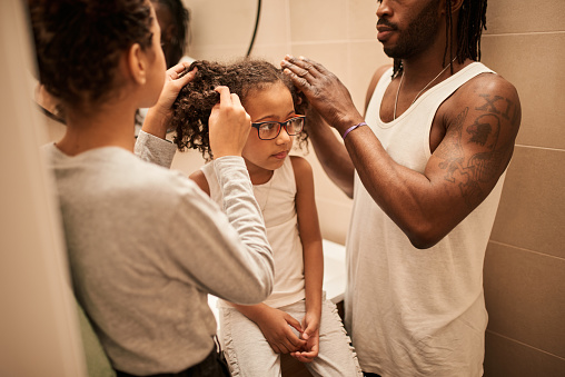Affectionate daddy and his teenage daughter is making hairstyle for little kid. He is using hairbrush with concentration. Cute girl is sitting at the bathroom and smiling dreamily
